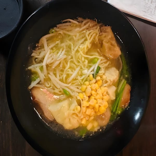 A black bowl of ramen with noodles, bean sprouts, corn, and sliced pork in broth.